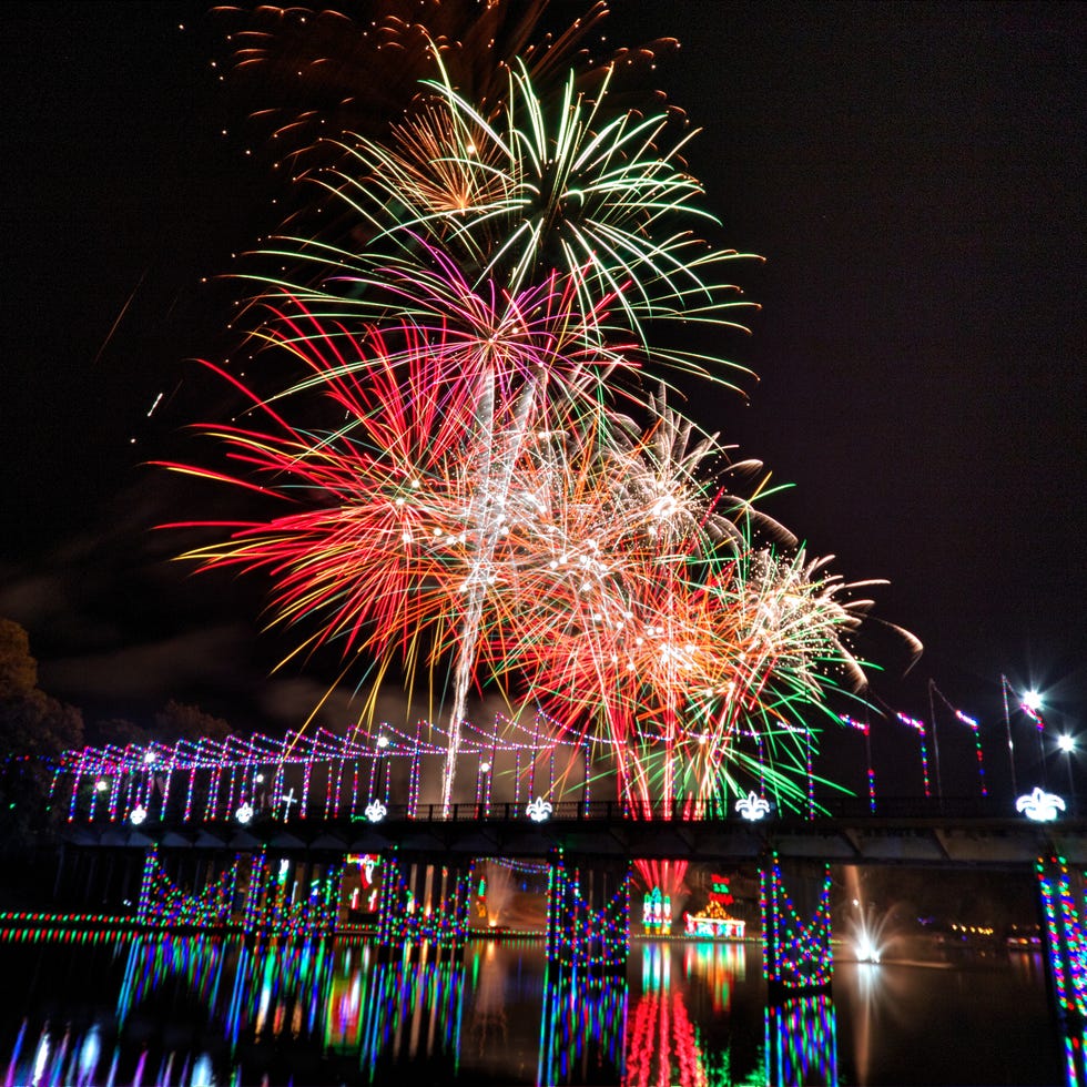 fuegos artificiales estallando sobre el río con un puente iluminado debajo con luces navideñas