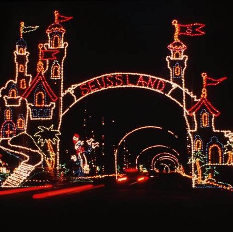 exhibición de luces que dice seussland en un arco con torreones de castillo a su alrededor y arcos de luces siguiéndolo