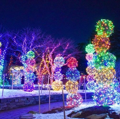 Globos iluminados de luces multicolores apilados uno encima del otro a lo largo de un camino nevado