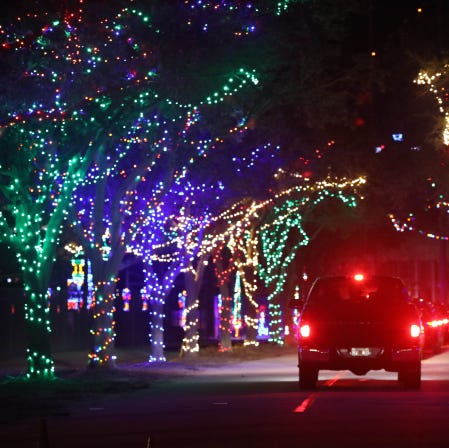 Coche circulando por la carretera con luces navideñas de colores brillantes colgadas de los árboles a ambos lados.